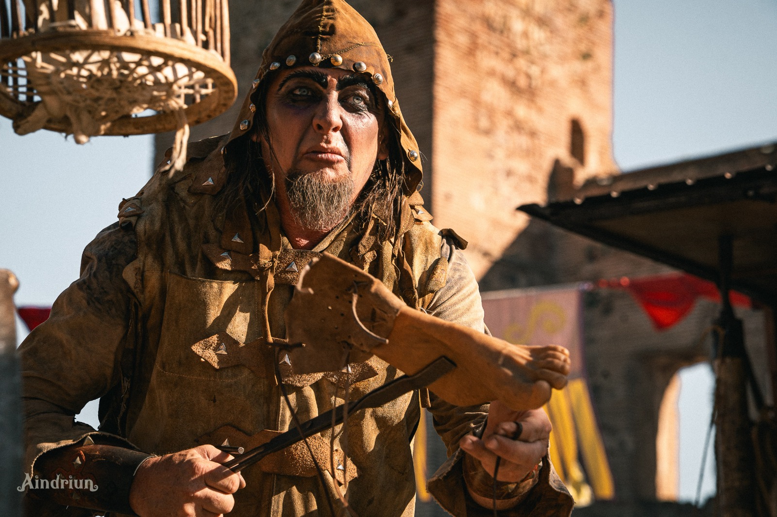 Personaje medieval encapuchado tocando un instrumento de cuerda ante una torre